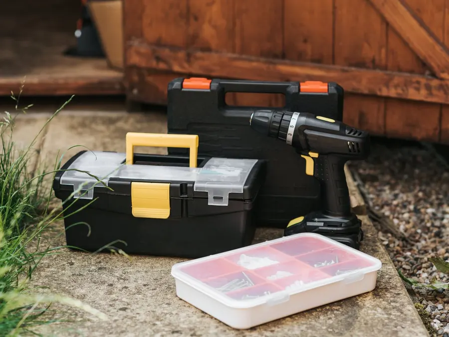 A cordless drill and toolbox staged outside a garage entrance, ready for a repair visit